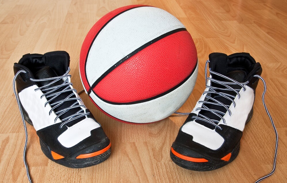A pair of high top sneakers and a basketball on a basketball court
