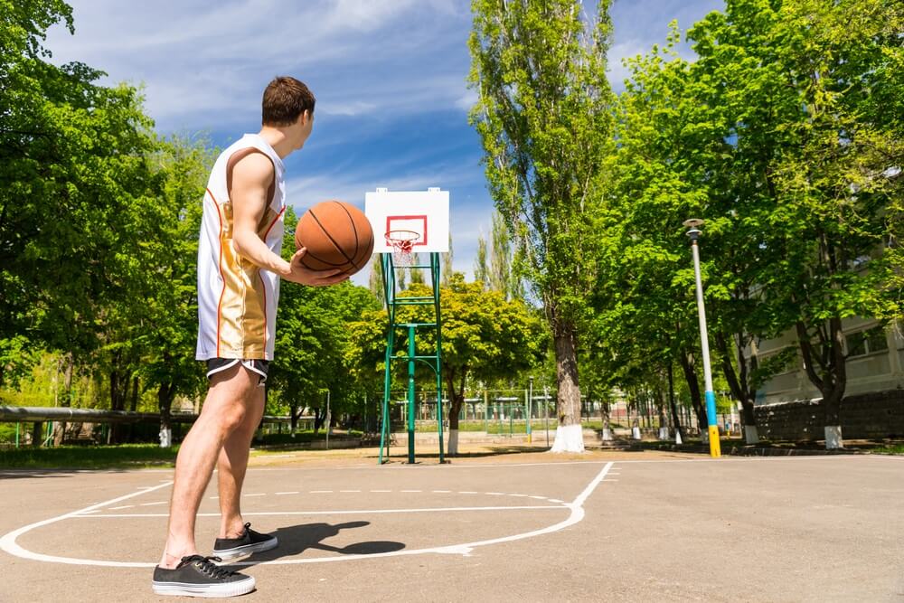 A young man stands on the top of the key on an outdoor basketball court
