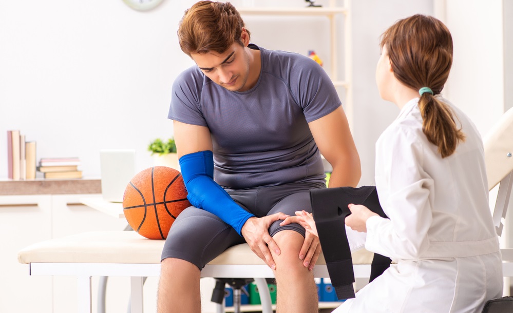 Young adult male basketball player visiting female doctor with knee pain