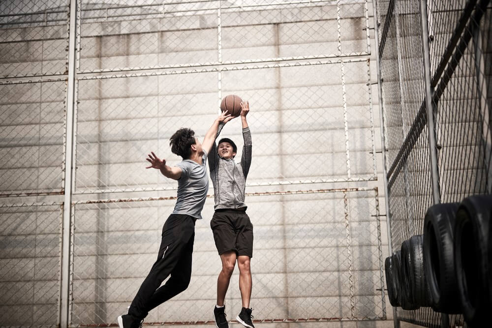 two young men playing basketball on an outdoor court
